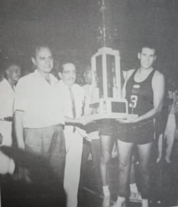 Team skipper Carlos (Caloy) Loyzaga receives the 1960 ABC title hardware from Yco team owner Don Manolo Elizalde, his boss with the Redshirts/Painters club, as PH coach Arturo Rius looks on.
