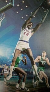 Towering Wilt Chamberlain of the Philadelphia (now Golden State) Warriors hauls down a rebound against Boston as the Celtics' John Havlicek looks on.