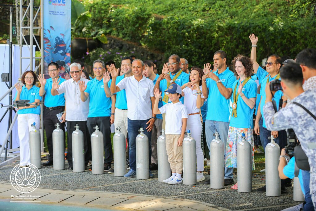 DOT Secretary Christina Garcia Frasco (middle, in white attire) shows the “love” sign while her fellow DOT officials, those from the local government of Mabini municipality and Batangas province, and ambassadors from Vietnam, South Korea, Malaysia, Sri Lanka, New Zealand and India, among others, cheer on during the launch of the inaugural Philippine Dive Experience program in popular dive destination Anilao in Mabini, Batangas on November 28, 2024. [Photo by the Department of Tourism]